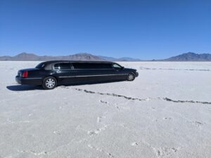 A sleek black limousine parked in a vast, dry desert with a clear blue sky.
