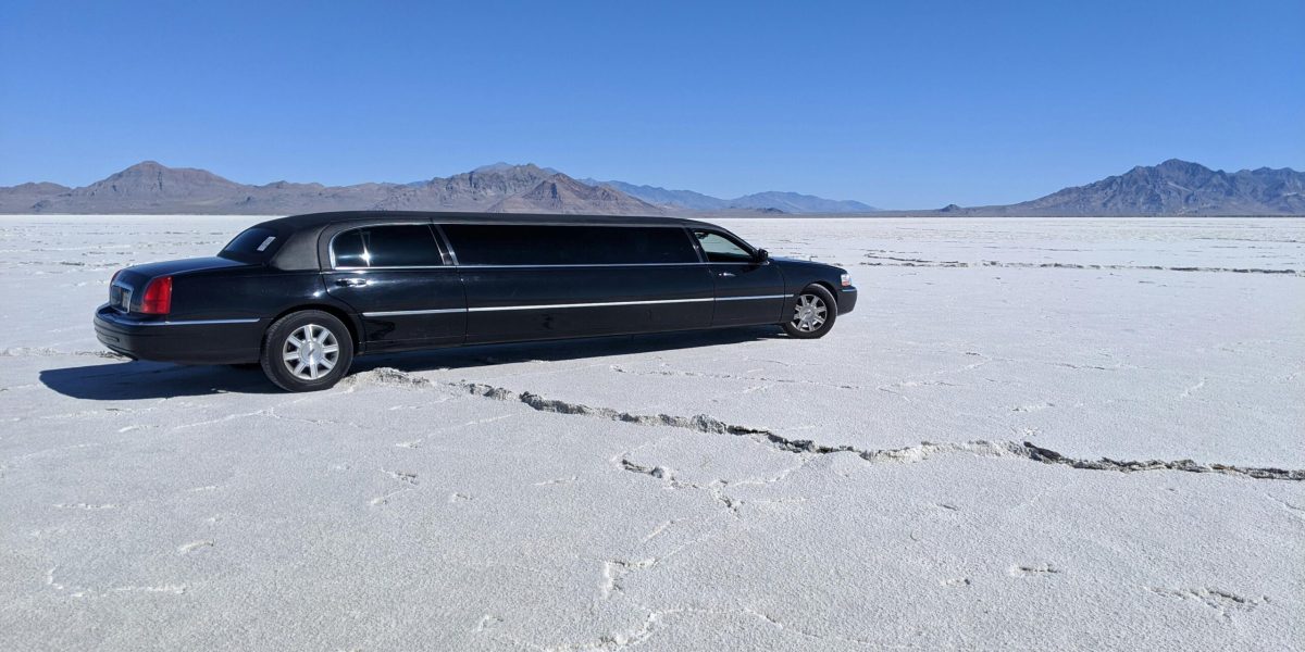 A sleek black limousine parked in a vast, dry desert with a clear blue sky.